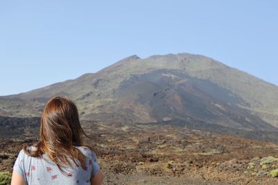 Rear view of woman looking at mountains against clear sky