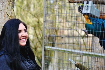 Smiling young woman looking at macaw in cage 