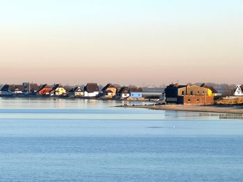 Houses by sea against clear sky during sunset