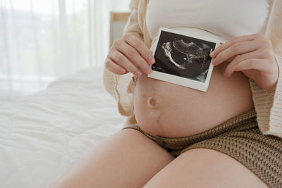 Midsection of woman using mobile phone while lying on bed at home