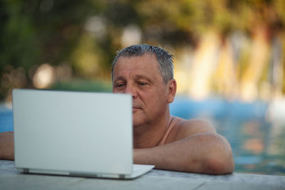 Mature man looking at laptop while swimming in pool