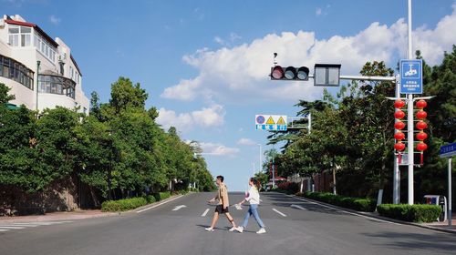People on road amidst trees against sky in city