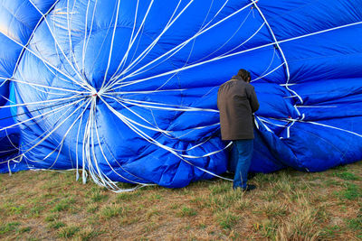 Rear view of man standing against blue hot air balloon on field