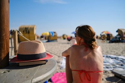 Rear view of carefree woman with backless bikini sitting on beach