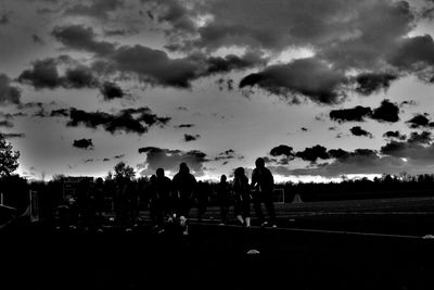 Silhouette people on field against sky during sunset