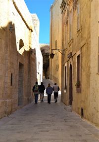 Rear view of people walking in alley amidst buildings