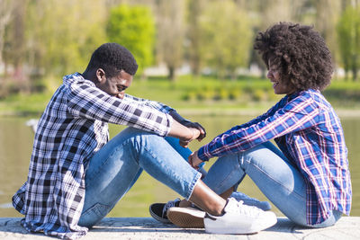 Side view of happy young couple sitting on retaining wall against lake