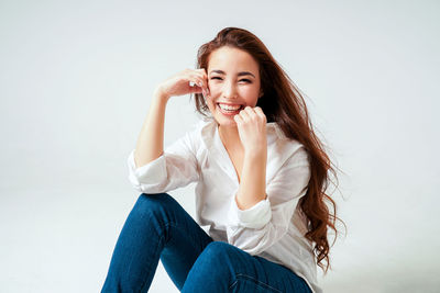 Portrait of smiling young woman sitting against white background