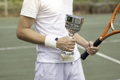 Young unrecognizable amateur tennis player holding an award winning cup on a tennis court