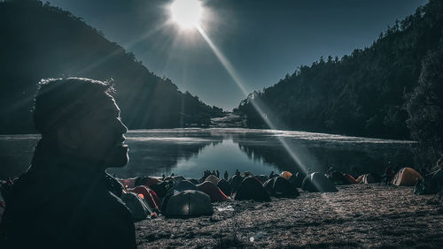 People by lake against sky on sunny day