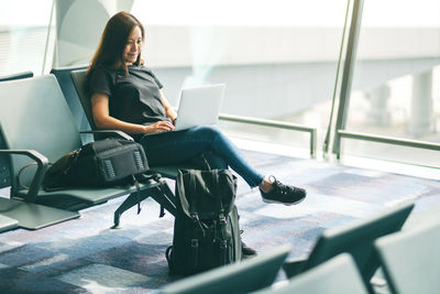 Smiling woman using laptop while sitting on chair at airport