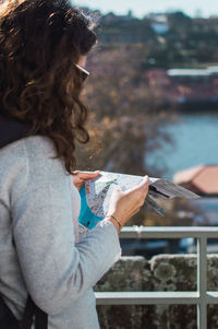 Side view of woman reading map while standing by railing