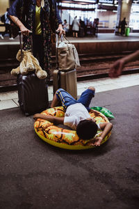 Boy lying on inflatable ring while mother standing with luggage at railroad station platform