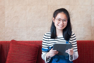 Portrait of smiling young woman using smart phone on sofa