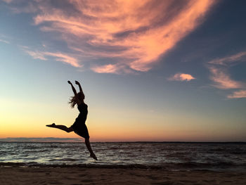 Silhouette of woman jumping on beach at sunset