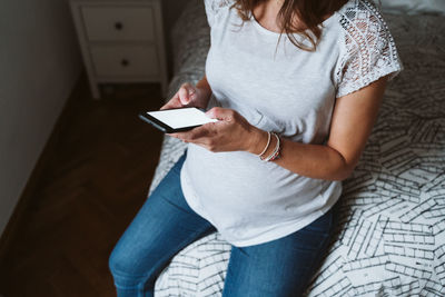 Midsection of pregnant woman using phone while resting at home