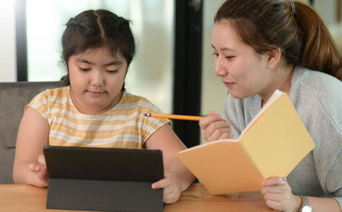 Asian girl studying privately with tutor at home, siblings teaching homework, online learning.