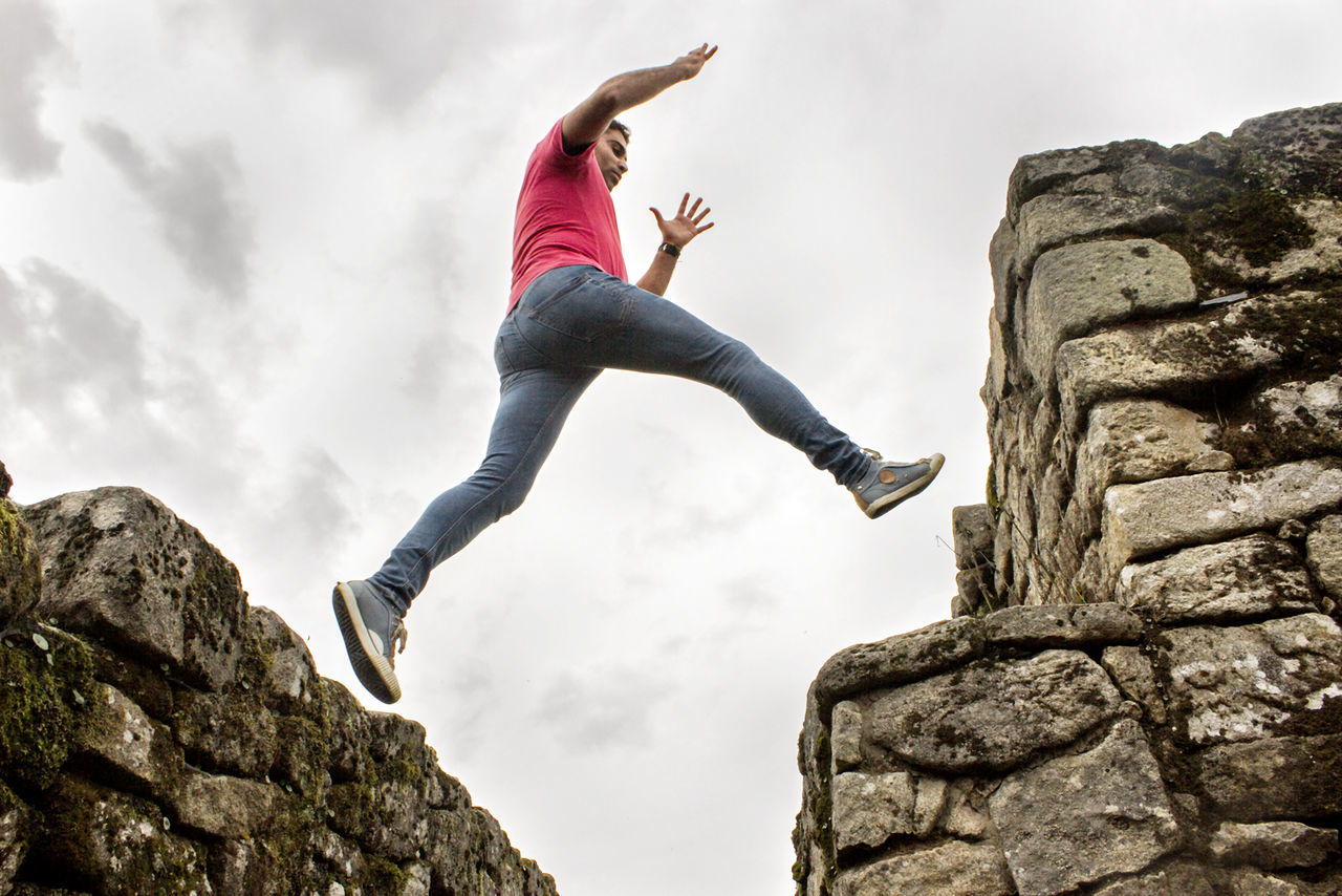 LOW ANGLE VIEW OF PERSON JUMPING ON ROCK