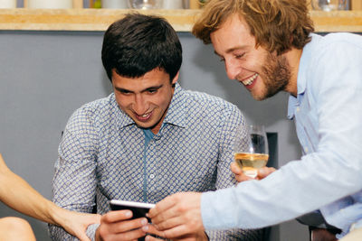 Smiling friends using mobile phone in restaurant