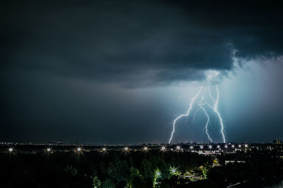 Lightning over illuminated cityscape against sky at night