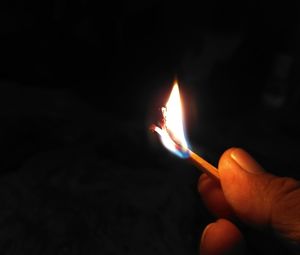 Close-up of hand holding lit candle in the dark