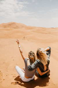 People sitting on sand dune in desert against sky