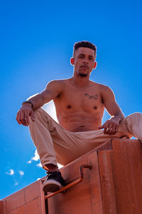 Low angle view of shirtless man against blue sky