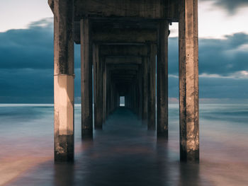 Pier on sea against cloudy sky during sunset