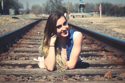 Portrait of smiling young woman lying on railroad track