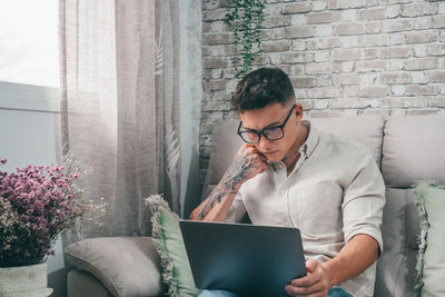 Young man using laptop while sitting on sofa at home