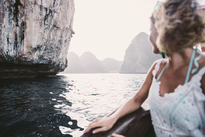 Woman sitting on rock by sea against mountains