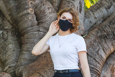 Portrait of young woman while standing against tree