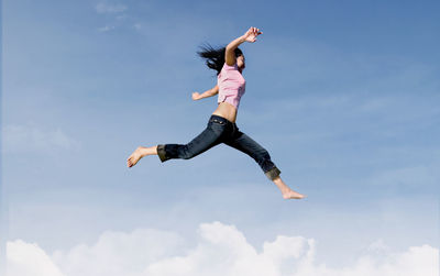 Low angle view of woman jumping against sky