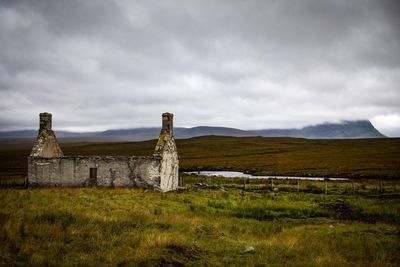 Old ruins on grassy field against cloudy sky