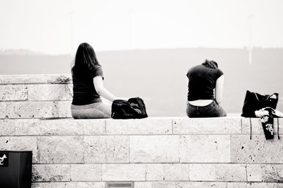 Rear view of women sitting against wall