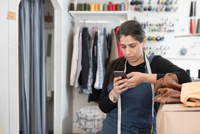 Mature female entrepreneur standing by cardboard box while using smart phone at laundromat