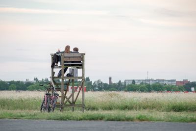 Rear view of friends on wooden structure over field against sky