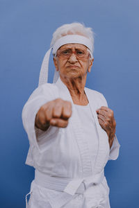 Portrait of senior woman doing karate against blue background