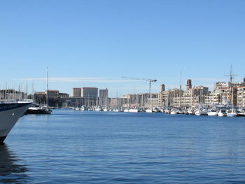 Sailboats in sea by buildings against clear blue sky