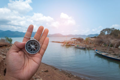 Cropped image of person holding navigational compass against river