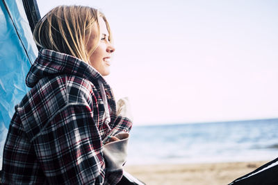 Side view of young woman sitting in tent at beach