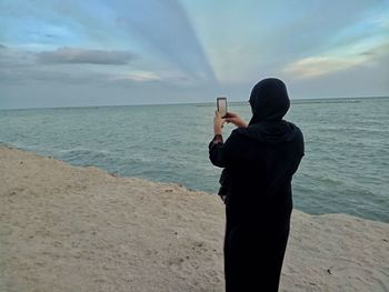 Man photographing at beach against sky