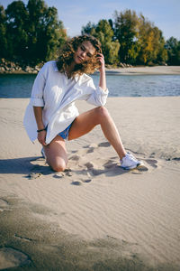 Young woman kneeling on sand against sea at beach