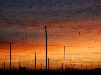 Silhouette electricity pylons on field against sky during sunset