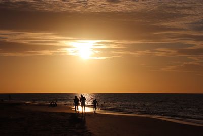 Silhouette people on beach against sky during sunset