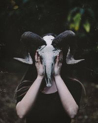 Woman covering face with animal skull while standing on field