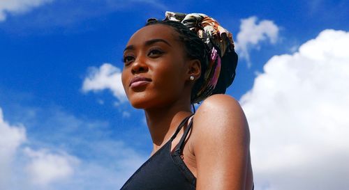 Low angle portrait of young woman looking away against sky