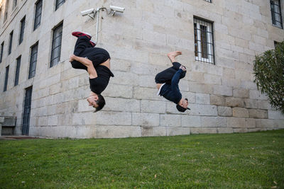 Full length of male friends jumping against building at lawn