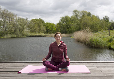 Beautiful young woman meditates in lotus position doing yoga in nature near the pond, yoga outdoor