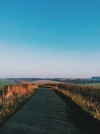 Road passing through field against clear sky